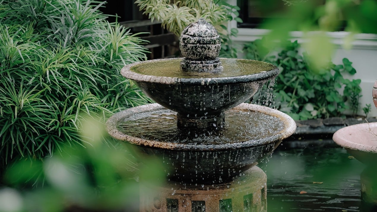 Two-level water fountain set against a backdrop of shrubbery.