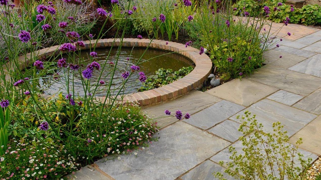 Tranquil pond next to a patio and flowers.