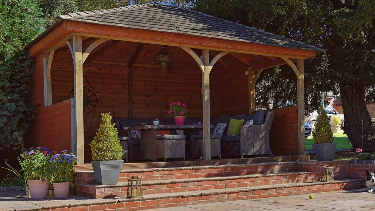 Wooden summer house covering a seating area with outdoor chairs and a table.