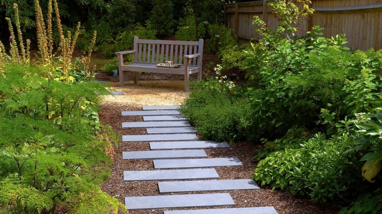 Narrow paving slabs laid as stepping stones out to a bench.