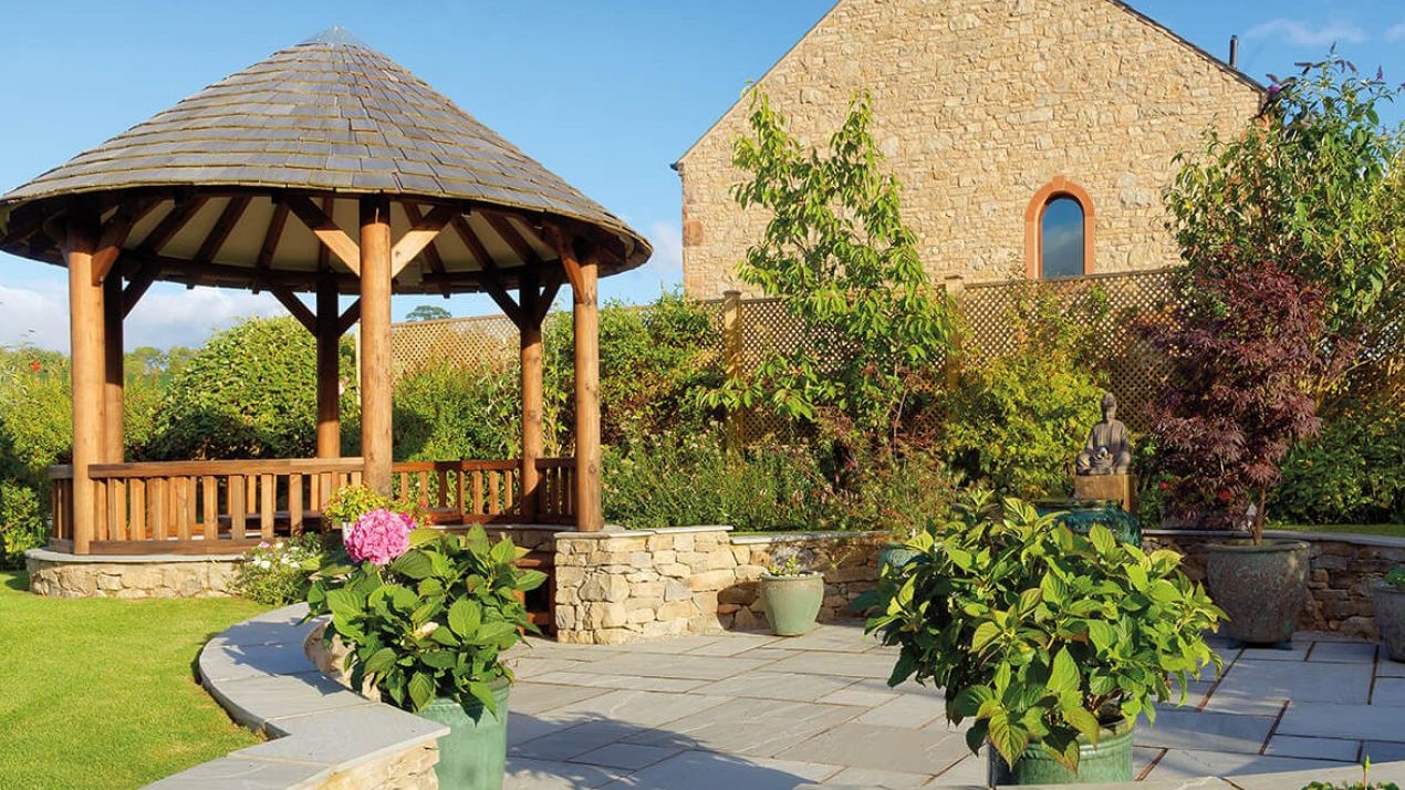 Wooden gazebo with tiled roof over an area of patio and seating.