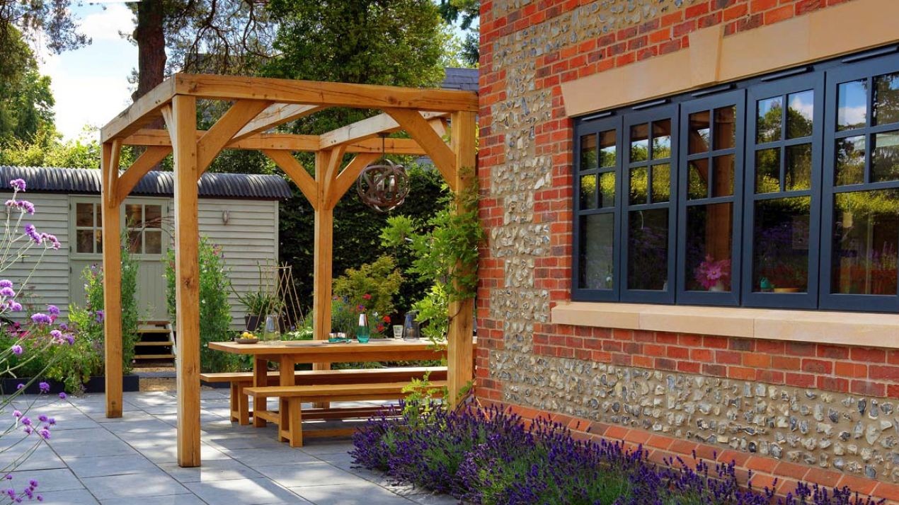 Wooden pergola frame with hanging light over a bench table.